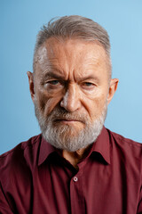 Obraz premium Portrait of handsome serious senior gray haired man looking at camera isolated on blue background