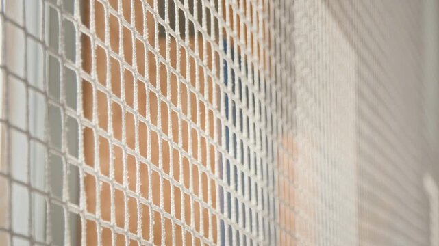 Minimal background shot of school gymnasium with focus on protective netting creating graphic square pattern against colorful walls, no people, copy space