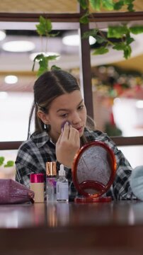 Beauty routine scene, Teen girl carefully retouching makeup with mirror and wipes nearby, Young woman softly enhancing her eye makeup amidst mall setup with natural elements and cosmetic items