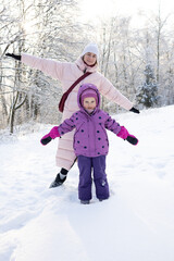 Close up of cute little girl in pink hat and purple suit looking at camera in winter forest
