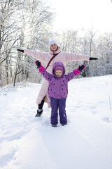 Happy mother and little daughter spreading arms like wings in beautiful snowy winter forest
