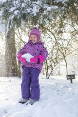 Cute little girl in purple winter overalls playing and crawling in deep white snow in sunny forest