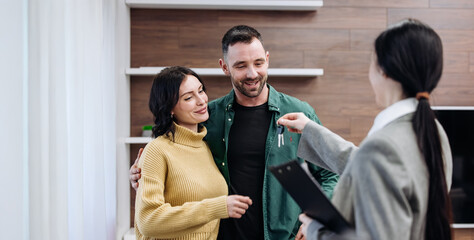 Couple receiving house keys from realtor inside modern living room with wooden accents and bright natural light during property handover ceremony with copy space