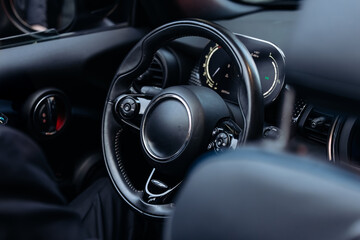 Close-up view of a modern car interior featuring a black steering wheel, dashboard controls, and digital display, highlighting the sleek design and technology of the vehicle