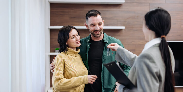 Couple receiving house keys from realtor inside modern living room with wooden accents and bright natural light during property handover ceremony with copy space
