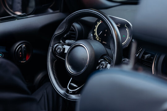 Close-up view of a modern car interior featuring a black steering wheel, dashboard controls, and digital display, highlighting the sleek design and technology of the vehicle - Powered by Adobe