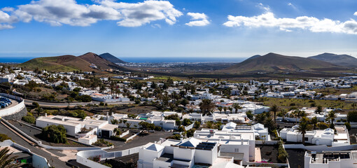 Whitewashed village on Lanzarote near La Geria, flat roofs and palm streets sit by black lava fields and rounded cones, with the Atlantic on the horizon in crisp light. © Aerial Film Studio