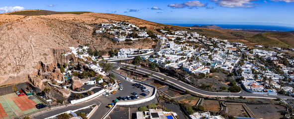 Aerial view of Nazaret on Lanzarote shows Lagomar Casa Museo in volcanic cliffs, white cubic homes, palm lined streets, terraced roads, and the Atlantic on the horizon. © Aerial Film Studio
