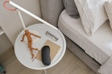 Nightstand holding everyday items and a creative wooden mannequin next to a comfortable bed