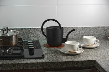 Black teapot and two white ceramic cups resting on granite countertop, ready for serving