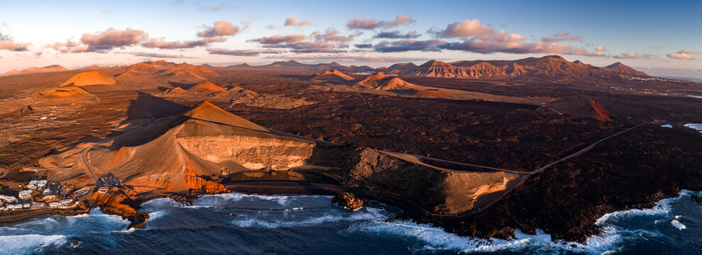 Aerial view of Timanfaya National Park on Lanzarote, Canary Islands, with cinder cones, lava fields, El Golfo and Los Hervideros coast, ribbon road, and Ajaches ranges at sunrise.
