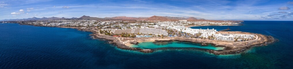 Aerial view of Puerto del Carmen on Lanzarote shows whitewashed hotels on a rocky peninsula, a...