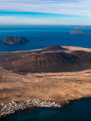 Aerial view shows cone shaped craters, lava flows, and a whitewashed village by a rocky bay on northern Lanzarote, facing La Graciosa, Montana Clara, and Alegranza. © Aerial Film Studio