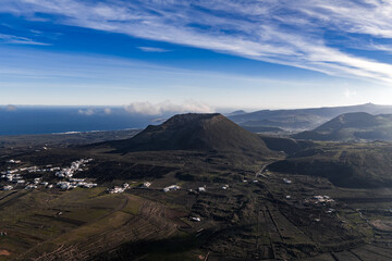 Aerial view of Lanzarote, Canary Islands, with a cinder cone, patterned lava, patchwork farmland, whitewashed villages, and the Atlantic along the left horizon. © Aerial Film Studio