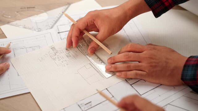 Professional engineer team discussion about house design on meeting table with architectural equipment and building blueprint scatter around at modern office. Focus on hand. Closeup. Delineation.