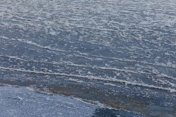 Fototapeta premium Frozen river texture with thin ice lines and snow crystals forming abstract winter background