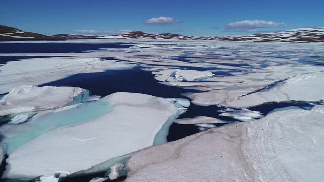 Aerial over a high mountain lake with large melting ice sheets and icebergs in Iceland.