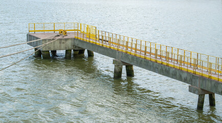 Concrete industrial pier with yellow railings on murky water. Mooring ropes attached to bollards. Minimalist maritime infrastructure for shipping and transport