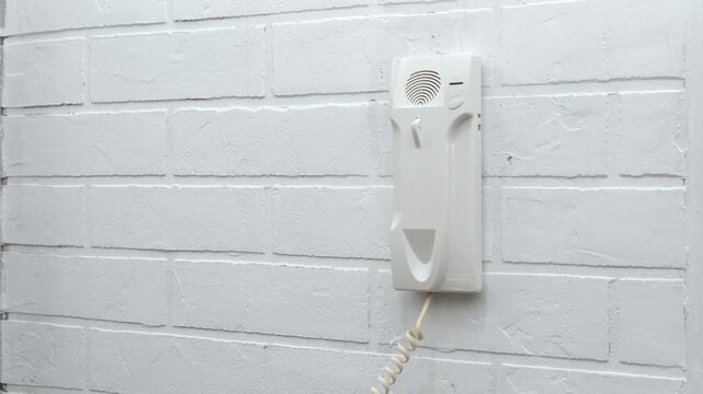 A man's hand lifts a white intercom telephone