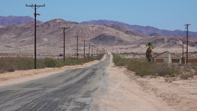 A road through the Mojave desert with abandoned houses nearby.