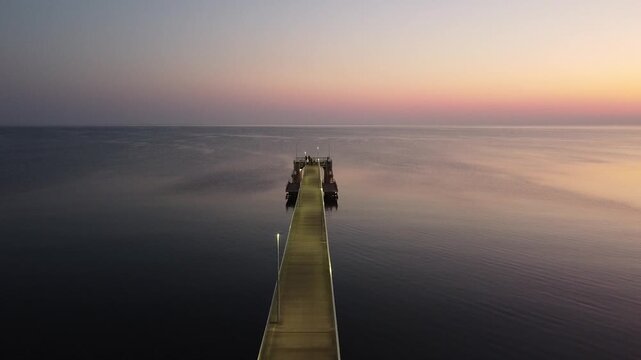 Symmetrical Pier Leading Into Calm Sea At Dusk, Illuminated Walkway Lights Create Vanishing Point, Small Silhouettes Gathered At Pier End, Serene Reflective Water, Cinematic Leading Lines