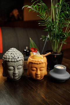 Colorful drinks served in decorative Buddha and monk cups at a cozy restaurant