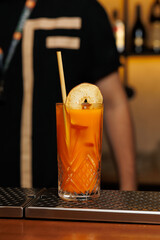 Refreshing cocktail served in a tall glass with a slice of fruit at a busy bar in the evening