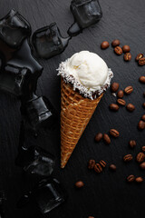 Ice cream cone with coconut flakes and coffee beans beside ice cubes on dark surface