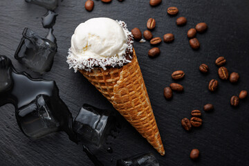 Delicious ice cream cone topped with coconut and served with coffee beans and ice cubes on a dark surface