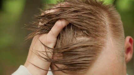 Young man adjusting damp hair, Rainy day park hair grooming, Man with damp hair adjusting his hairstyle after walk, Young individual carefully arranging wet fringe following rainy park visit
