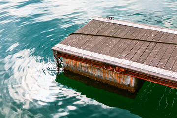 Floating dock on calm green water. Loose rope lies across wooden deck, adding texture to tranquil aquatic scene. Water ripples catching sunlight adjacent to the edge of a sturdy, functional boat slip