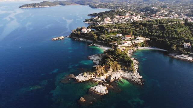 Aerial drone view of Kassiopi, coast sea village in northeast coast of Corfu island, Ionian Islands, Kerkyra, Greece in a summer sunny day, with marina, town, beach and castle, Greek landscape