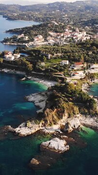 Aerial drone view of Kassiopi, coast sea village in northeast coast of Corfu island, Ionian Islands, Kerkyra, Greece in a summer sunny day, with marina, town, beach and castle, Greek landscape