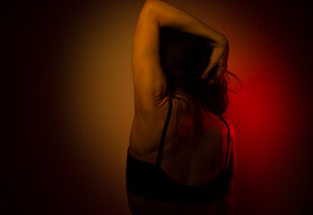 Obraz premium Woman sexual slim body posing in studio iridescent colorful artistic lighting glows in fantasy club neon creative rays. Magical blending light, color, fantasy with sexy female. Low key art. Back view