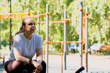 A woman taking a break during her outdoor workout session at a park fitness area on a sunny day