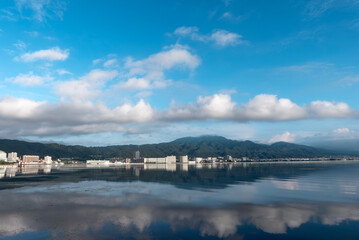 早朝の静かな琵琶湖　大津市のマンション群と雲が湖面に映る風景