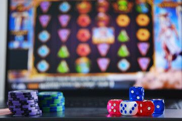 Dice and gambling token chips with an online slot gambling background on a laptop screen. Online gambling games. Gambling addiction. Gambling bets. © PANCASONA CREATION
