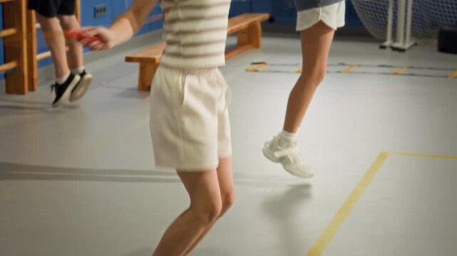Side view shot of two girls doing jumping rope exercises in indoor gym during PE lesson, focus flowing from face to legs, copy space