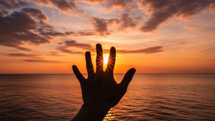 Silhouetted hand reaches to touch the sun's radiant burst over a calm ocean at vibrant sunset