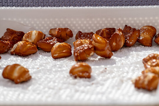 A large white plastic tray and liner filled with fresh soft pretzel bites. The sweet bread is coated in butter and sprinkled with sea salt. The mini pretzels have a dark brown outer crust. 
