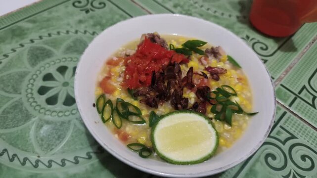 Barobbo Traditional Indonesian Bugis Corn Porridge Served with Chili Sambal Fried Shallots Green Onions and Lime Wedge in Bowl