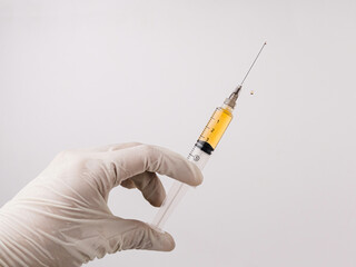 Close-up of a syringe with liquid vaccine dripping from the needle. A doctor or nurse wearing white medical gloves holds a syringe filled with vaccine, isolated on a white background.