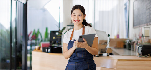  Portrait of asian tan woman barista cafe owner hodding tablet at the bar. SME entrepreneur seller...