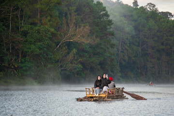 asian family by mother daughter tourist relax travel on bamboo rafting with selfie take photo by smartphone in lake with morning fog mist on water surface at Pang Ung Reservoir in winter Thailand
