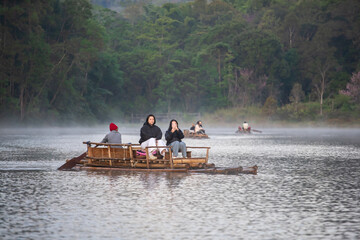 asian family by mother daughter tourist relax travel on bamboo rafting with selfie take photo by mobile phone in lake with morning fog mist on water surface at Pang Ung Reservoir in winter Thailand