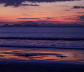 Sunset over the Andaman Sea from Tarutao Island, where soft sun rays illuminate the tranquil beach and distant islands.