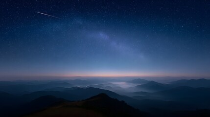 Fototapeta premium A serene night sky with countless stars and the Milky Way stretches above misty mountain ranges at twilight featuring a shooting star