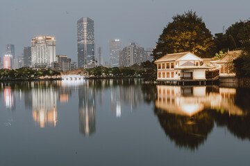 Fototapeta premium City Skyline and Traditional Pavilion Reflecting in Calm Lake at Dusk - Huizhou West Lake