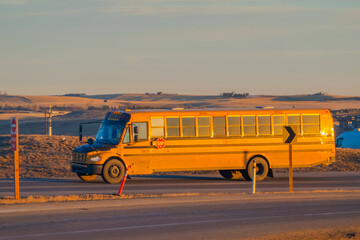 Yellow school bus driving on a rural highway at sunset with golden hour light reflecting off windows.