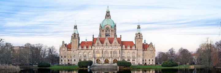 Obraz premium Stunning view of Hannover City Hall reflected in the tranquil waters of Maschsee Lake, framed by trees and clouds. A perfect representation of the city s beauty and architectural charm.